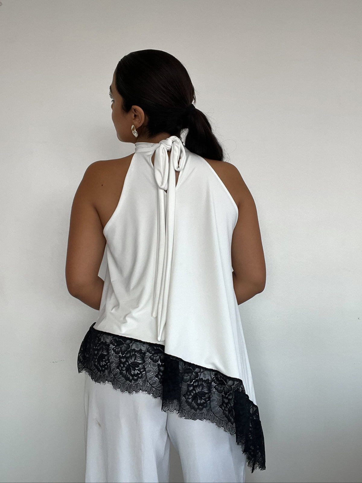 Top polera blanco halter asimétrico con detalle de encaje negro y amarras, diseño elegante para mujer